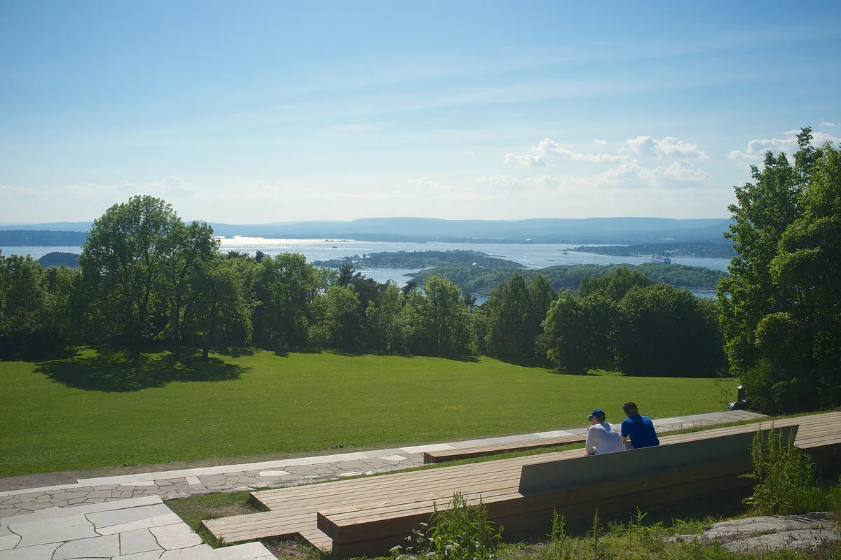 The lawn at Ekebergparken sloping towards the Oslo fjord, with wooden benches in the foreground and islands in the distance.