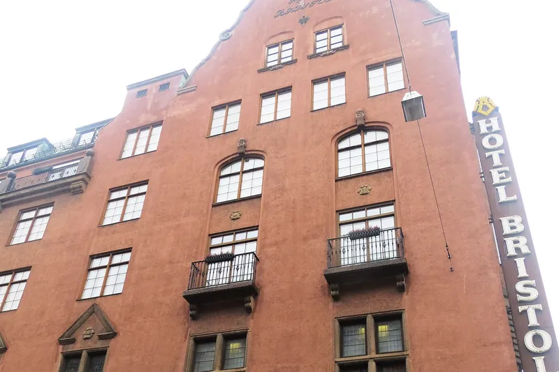 The red brick facade of Hotel Bristol with its curved gable, balconies and the hotel's vertical sign.